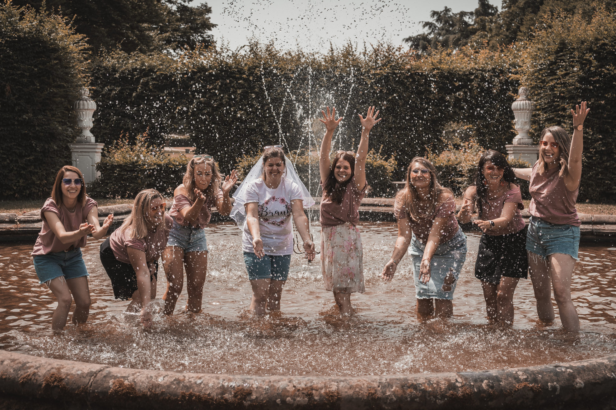 Freundinnen stehen beim Junggesellinnenabschied im Springbrunnen und spritzen Wasser hoch