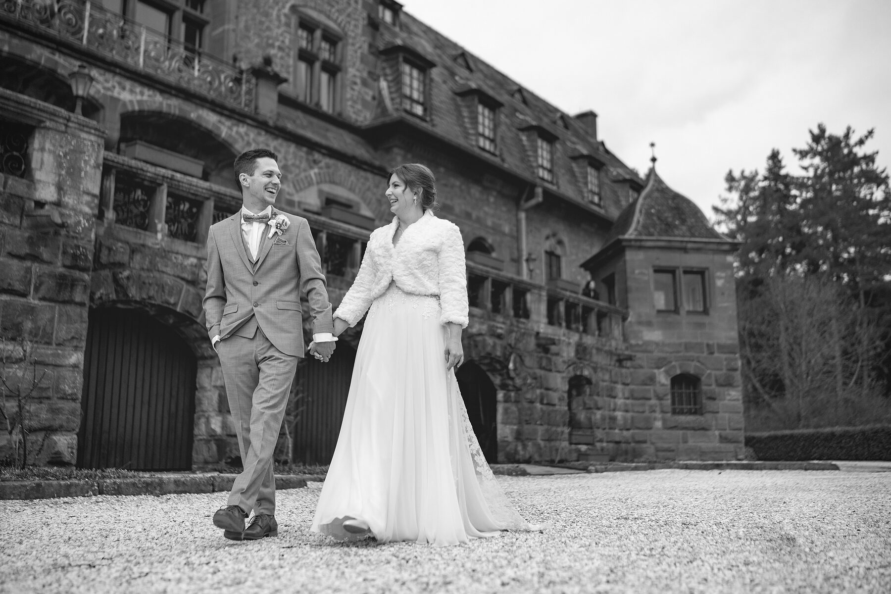 Brautpaar geht Hand in Hand vor einem Schloss, Schwarzweiß