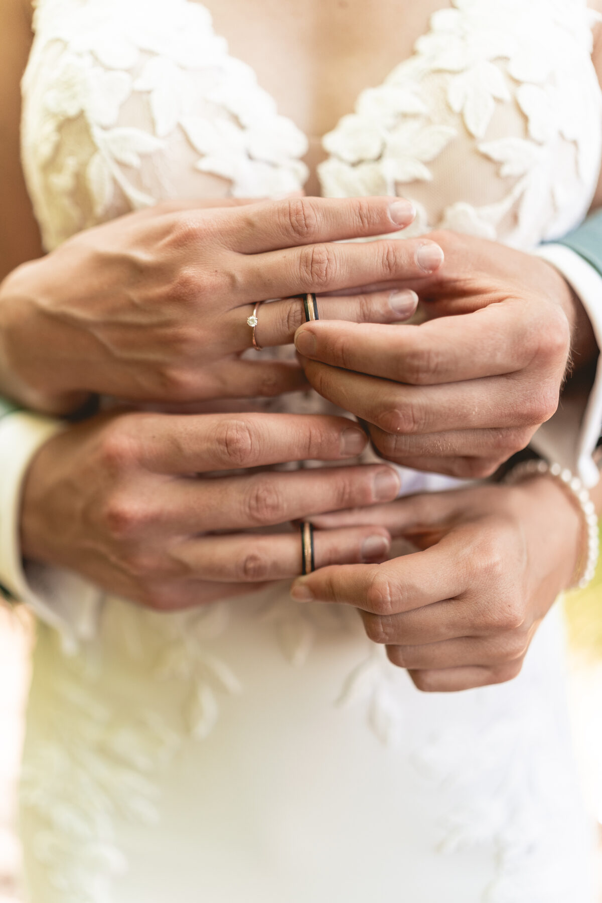 Hände des Brautpaars mit Eheringen vor dem Brautkleid